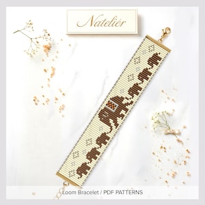 May include: A beaded loom bracelet featuring a repeating pattern of brown elephants on a cream background with small silver accents. The bracelet has gold-toned metal end bars and a lobster claw clasp. The text Natelier is visible above.