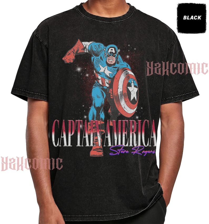May include: A black acid-wash t-shirt featuring a graphic of Captain America in a dynamic pose with a shield. The text CAPTAIN AMERICA and Steve Rogers is printed below the character. A small black box in the corner contains the word BLACK.