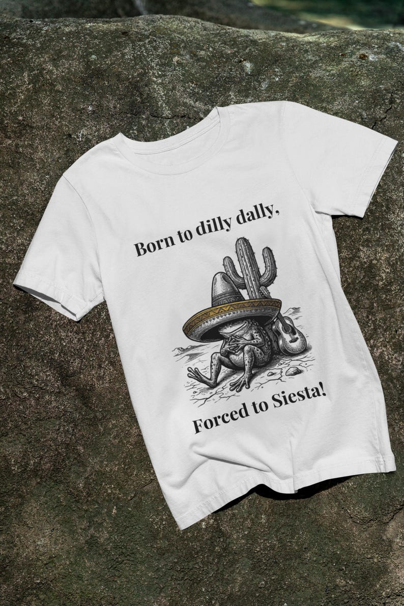 Puede incluir: Camiseta blanca con un dise&ntilde;o de una rana con sombrero apoyada en un cactus. El texto dice "Born to dilly dally, Forced to Siesta!" en negro. El dise&ntilde;o incluye una guitarra.