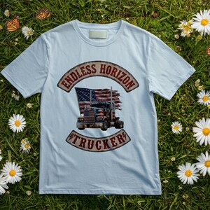 May include: A light blue t-shirt featuring a graphic print of a semi-truck with an American flag design. The text "ENDLESS HORIZON" is arched above the truck, and the word "TRUCKER" is arched below, both in a distressed, weathered red font.