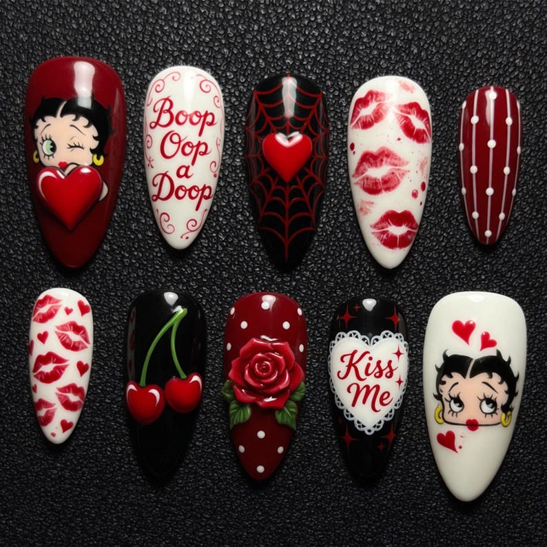 May include: A collection of ten artificial nails with various designs. The designs include Betty Boop, lips, hearts, cherries, a rose, and the text "Boop Oop a Doop" and "Kiss Me". The nails are in shades of red, black, and white.