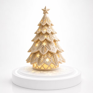 May include: A cream-colored ceramic Christmas tree with star and snowflake cutouts. The tree is topped with a star and sits on a white pedestal. The tree is lit from within, casting a warm glow through the cutouts.