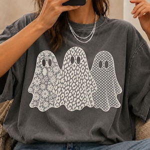 May include: A charcoal gray short-sleeve t-shirt featuring a graphic of three white ghosts. The left ghost has a floral pattern, the center ghost has a leopard print, and the right ghost has a polka dot pattern. The text reads COSMIC MOOD PNG 300DPI COMMERCIAL USE.
