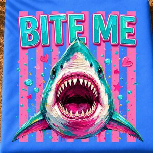 May include: A blue fabric print featuring a shark with an open mouth and sharp teeth. The text BITE ME appears in teal above the shark. The background consists of vertical pink stripes, small pink hearts, teal bubbles, and a pink star.