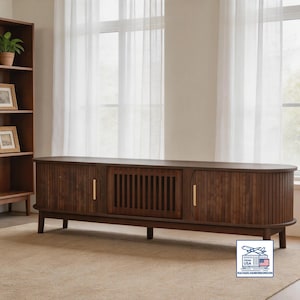 May include: A dark brown wooden media console with a curved front and vertical grooved detailing. It has two doors with gold handles and a central section with vertical slats. The console is on short, dark legs.