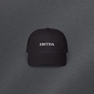 May include: Black baseball cap featuring the white word "EBITDA" on the front. The cap has a curved peak and a classic six-panel design. The hat is made of a soft, durable material.