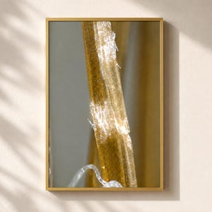 May include: A vertical rectangular wall art piece featuring a gold-toned frame. The artwork displays a close-up, abstract composition of a textured, amber-colored vertical element with crystalline highlights and a thin, translucent wire.