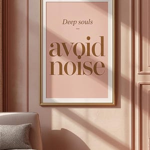 Può includere: Una stampa artistica incorniciata con le parole "Deep souls avoid noise" in una cornice dorata. L'opera d'arte è esposta su una parete rosa, con una poltrona e un tavolino abbinati in primo piano. La stanza è decorata in tonalità rosa.