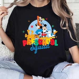 May include: A black t-shirt featuring a graphic of Disney characters Goofy, Mickey Mouse, Pluto, and Donald Duck against a light blue circle. The text "PRESCHOOL Squad" is printed below in colorful, bold, and script lettering with star accents.