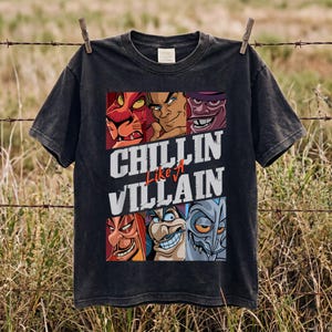 Pode incluir: Uma t-shirt preta de manga curta com uma impressão gráfica de seis vilões animados dispostos em duas filas. O texto "CHILLIN Like A VILLAIN" está impresso em letras grandes brancas e vermelhas no centro da t-shirt, entre os painéis.