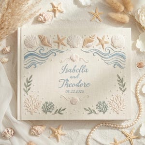 May include: A cream-colored wedding guest book with embroidered seashells, starfish, and waves. The names "Isabella and Theodore" and the date 08.22.2025 are embroidered in blue. The book is surrounded by seashells and pearls.