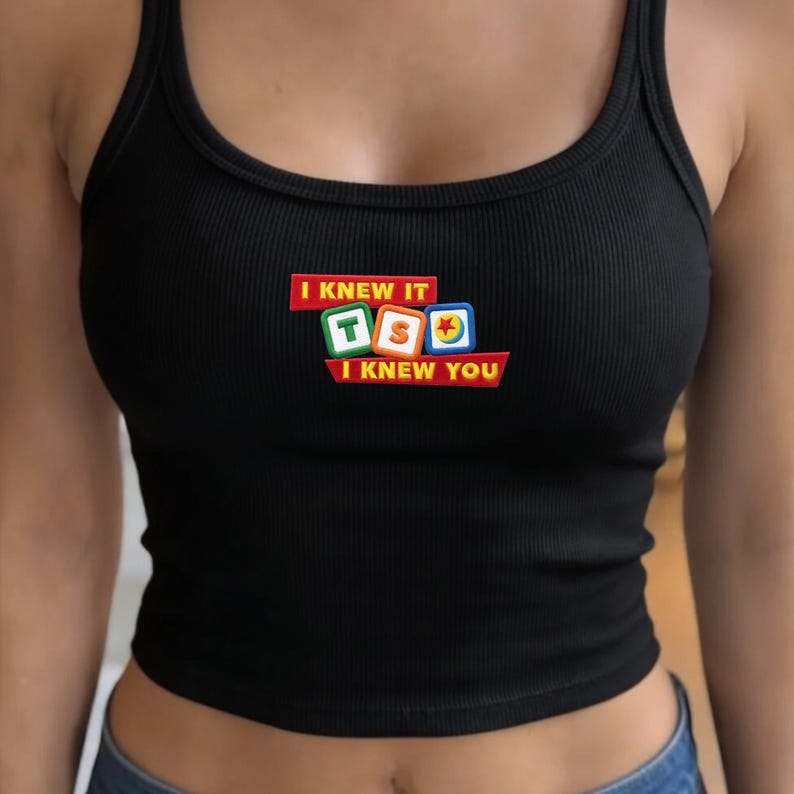 May include: A black ribbed tank top featuring a central graphic with the text I KNEW IT and I KNEW YOU in yellow letters on red rectangular backgrounds, surrounding three colorful square blocks displaying the letters T, S, and a red star icon.
