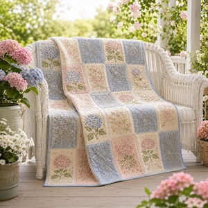 May include: A patchwork quilt featuring a repeating grid pattern of light blue, cream, and soft pink squares. The design includes embroidered hydrangea flower motifs in blue and pink, interspersed with small floral print blocks in coordinating colors.