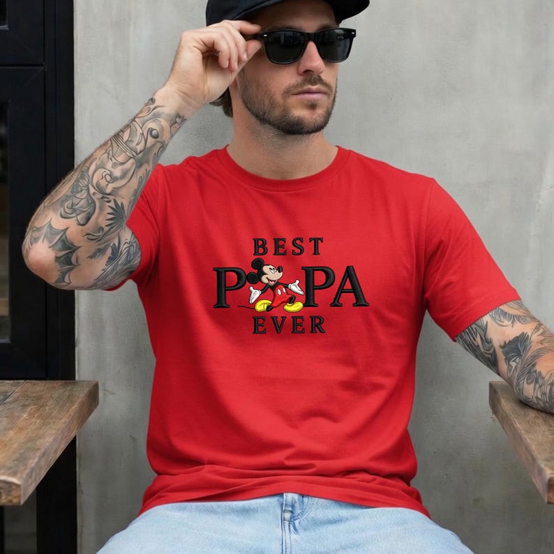 Puede incluir: Una camiseta roja con las palabras "BEST PA PA EVER" en letras negras y un gr&aacute;fico de Mickey Mouse. La camiseta es de manga corta y est&aacute; hecha de un material suave.