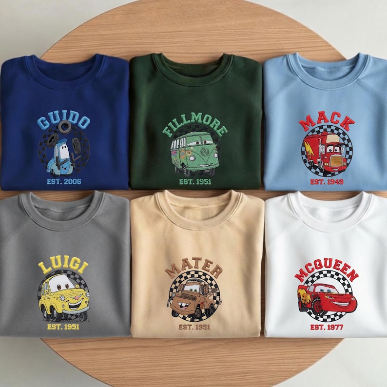 May include: Six crew neck sweatshirts in various colors, each embroidered with a character from the movie Cars. The sweatshirts feature characters like Guido, Fillmore, Mack, Luigi, Mater, and McQueen, with their names and the year they were established.
