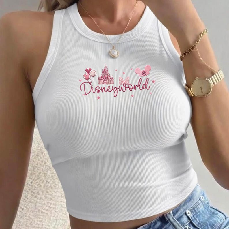 Peut inclure: D&eacute;bardeur blanc c&ocirc;tel&eacute; avec un motif Disneyworld rose. Le motif comprend un ch&acirc;teau, des ballons et le texte Disneyworld. Le d&eacute;bardeur a un col rond et une coupe ajust&eacute;e.