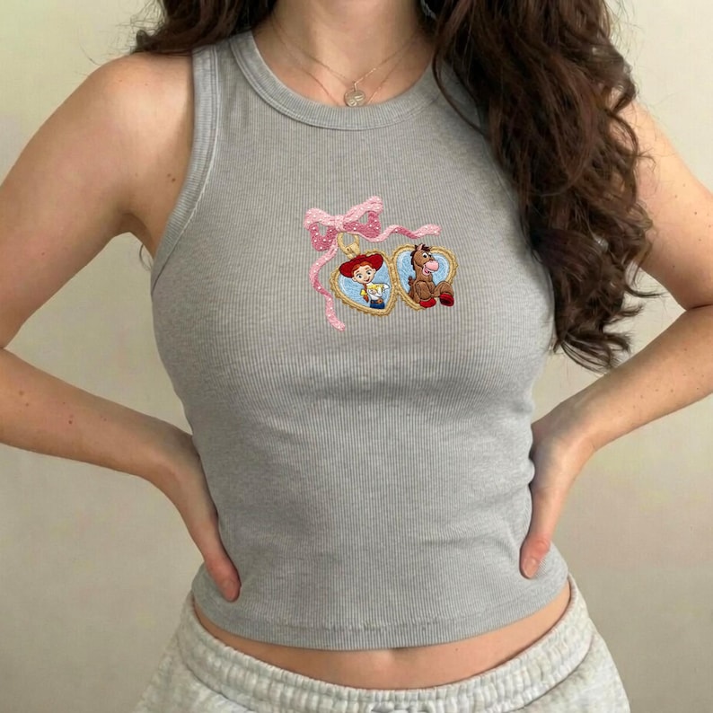 May include: Gray ribbed tank top with a pink bow and two heart-shaped embroidered patches. One patch features a cartoon girl, the other a brown horse. The tank top is sleeveless.