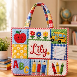 May include: A quilted tote bag featuring a patchwork design with school-themed appliqués including a smiling red apple, colorful flowers, a yellow school bus, the name Lily in red script, a notebook page, ABC letters, pencils, and crayons.