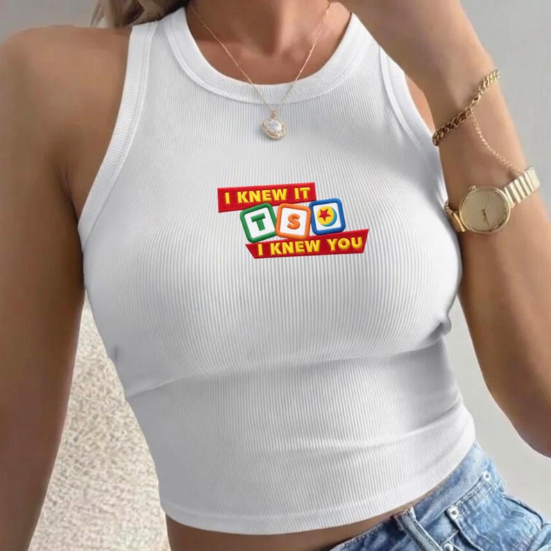 May include: A white ribbed tank top featuring a graphic print with the text I KNEW IT I KNEW YOU in red banners, accompanied by three colorful square blocks displaying the letters T, S, and a ball icon in the center of the chest area.