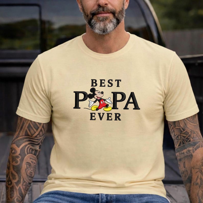 Puede incluir: Camiseta color crema con el texto "BEST PA EVER" y un gr&aacute;fico de Mickey Mouse. El gr&aacute;fico muestra a Mickey Mouse en una pose cl&aacute;sica, con pantalones cortos rojos, zapatos amarillos y guantes blancos. La camiseta tiene mangas cortas.