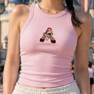 Puede incluir: Camiseta sin mangas rosa claro con dise&ntilde;o de dibujos animados de una vaquera montando a caballo. El dise&ntilde;o es en tonos marrones, rojos y blancos. La camiseta sin mangas tiene cuello redondo y sin mangas.