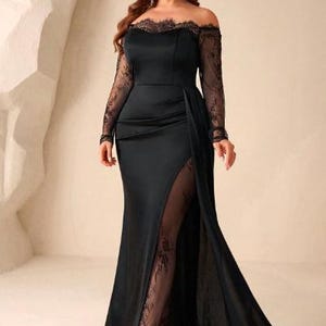 May include: A floor-length black gown featuring an off-the-shoulder neckline with delicate lace trim, long sheer lace sleeves, and a fitted bodice. The skirt includes a high side slit that reveals a sheer lace panel underneath the satin fabric.
