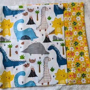May include: Two pieces of fabric. One features a white background with blue, yellow, and brown dinosaurs, volcanoes, and palm trees. The other has a yellow background with white and orange flowers.
