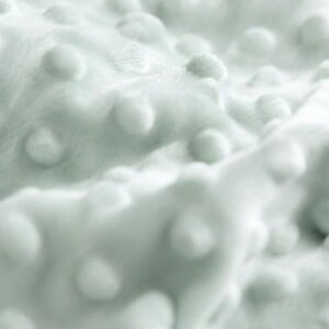 May include: A soft, light mint green fabric featuring a raised, textured dot pattern across the entire surface. The material has a plush, velvety appearance with consistent, evenly spaced circular bumps that create a tactile, three-dimensional effect.