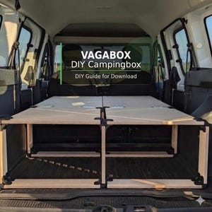 Può includere: Un telaio modulare per box da campeggio in legno chiaro installato nel retro di un veicolo. Il testo VAGABOX DIY Campingbox DIY Guide for Download è sovrapposto all'immagine. La struttura presenta pannelli piatti, cerniere metalliche e angolari neri.