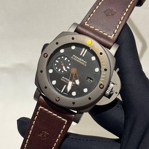 May include: A Panerai Submersible automatic watch with a dark gray face, a brown leather strap, and a rotating bezel. The watch has white and gold accents, a date display, and is water resistant to 300m.