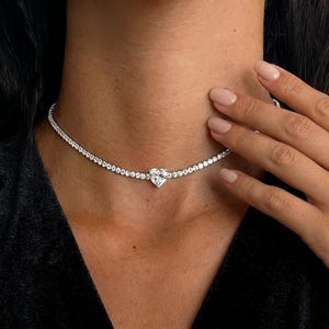Puede incluir: Un delicado collar de diamantes con un colgante en forma de corazón. El collar está compuesto por pequeños diamantes redondos muy juntos, creando un efecto brillante. El colgante de corazón es el punto focal, añadiendo un toque romántico a la joya.