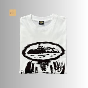 May include: A white short-sleeved t-shirt featuring a black graphic print on the chest. The design depicts a stylized, oval-shaped landscape or island silhouette above two hands reaching upward, rendered in a high-contrast, textured black ink style.
