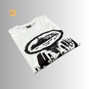 May include: A white short-sleeved t-shirt featuring a large, bold black graphic print on the front. The design consists of a textured, abstract circular shape with radiating lines, creating a high-contrast visual effect on the fabric.