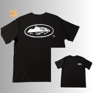 May include: A black short-sleeve t-shirt featuring a large white oval graphic on the back containing a silhouette of a cruise ship. A smaller version of the same white oval cruise ship graphic is positioned on the front left chest area of the shirt.