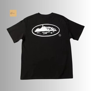 May include: A black short-sleeve t-shirt featuring a white graphic on the back. The graphic consists of an oval outline containing a white silhouette of a ship on water, with a small registered trademark symbol located to the right of the oval.