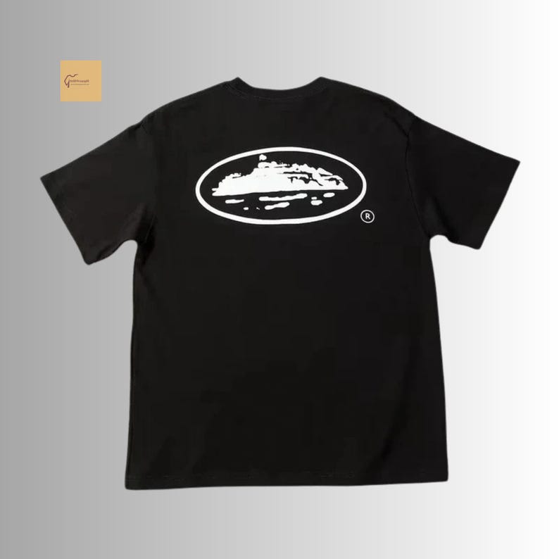May include: A black short-sleeve t-shirt featuring a white graphic on the back. The graphic consists of an oval outline containing a white silhouette of a ship on water, with a small registered trademark symbol located to the right of the oval.