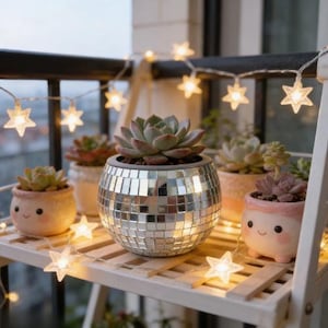 Può includere: Una collezione di piante grasse in vasi decorativi, tra cui un vaso in stile discoteca e altri con facce carine. Le piante sono su una mensola di legno bianco, illuminate da una stringa di luci a forma di stella. Tema: arredamento per la casa.