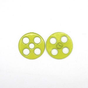 May include: Two circular lime green buttons, each featuring a central hole surrounded by four additional circular cutouts arranged in a square pattern. The buttons have a smooth, flat surface and a distinct, uniform bright green colour throughout.