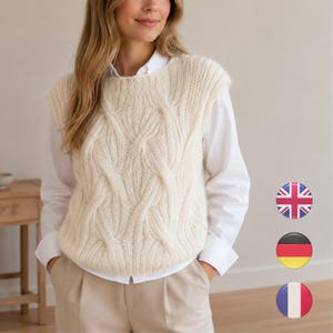 May include: A cream-coloured cable knit sweater vest featuring a thick, textured braided pattern on the front. The sleeveless garment has a round neckline and is layered over a crisp white long-sleeved button-down shirt and light tan trousers.