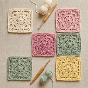 Könnte beinhalten: Eine Sammlung farbenfroher, quadratischer Häkelstücke in Creme, Rosa, Grün und Gelb. Zwei Häkelnadeln und Wollknäuel sind ebenfalls vorhanden. Die Häkelquadrate weisen ein detailliertes Blumendesign auf.