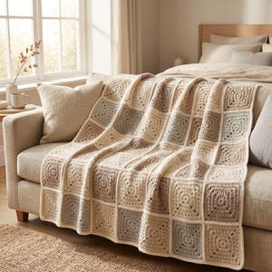 Peut inclure: Une couverture en crochet beige et grise drap&eacute;e sur un canap&eacute;. La couverture est compos&eacute;e de panneaux carr&eacute;s de diff&eacute;rentes nuances de beige et de gris. Le canap&eacute; est de couleur neutre, et la couverture ajoute une touche chaleureuse et faite &agrave; la main &agrave; la pi&egrave;ce.