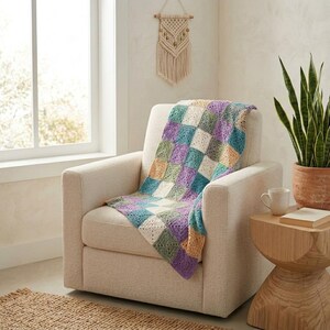 Peut inclure: Un fauteuil cr&egrave;me avec une couverture crochet&eacute;e &agrave; carreaux color&eacute;s. La couverture pr&eacute;sente des carr&eacute;s bleus, verts, violets et cr&egrave;me. Une petite table d'appoint en bois avec une tasse et un livre. Un macram&eacute; est visible.
