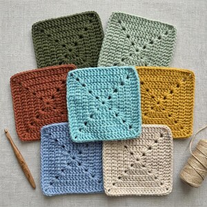 Peut inclure: Un ensemble de sept carr&eacute;s granny crochet color&eacute;s dans des tons de vert, rouille, bleu, jaune et cr&egrave;me. Un crochet en bois et une pelote de ficelle sugg&egrave;rent un th&egrave;me artisanal.