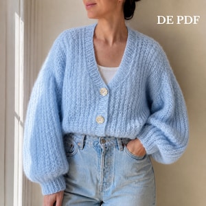 Peut inclure: Un cardigan bleu clair à col en V avec une texture en maille côtelée duveteuse, des manches longues bouffantes et deux gros boutons blancs sur le devant. Le vêtement est porté sur un haut blanc et un jean bleu clair. Le texte DE PDF est visible.