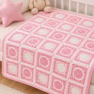 Könnte beinhalten: Eine handgefertigte, rosa und weiße Häkeldecke für Babys. Die Decke hat ein sich wiederholendes quadratisches Muster mit einem zentralen kreisförmigen Design in jedem Quadrat. Die Decke wird auf einem Kinderbett mit einem rosa sternförmigen Kissen und einem Teddybären präsentiert.