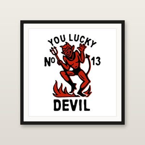 May include: A framed square print featuring a red devil character holding a trident, standing above flames. The text reads YOU LUCKY No 13 DEVIL in bold black lettering. The design is centred on a white background within a thin black frame.