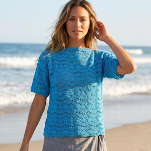 Pode incluir: Uma blusa de manga curta em azul brilhante com um padrão intrincado de crochê em ponto concha repetitivo. A peça tem um decote largo e reto e um corte descontraído, com o design de malha texturizada criando um efeito visual ondulado.