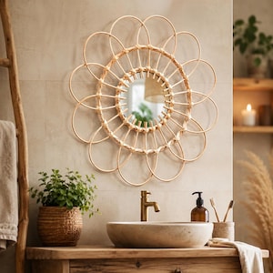 May include: A round, woven rattan mirror with a floral design hangs above a wooden vanity. The mirror's frame is made of light brown rattan, and the vanity features a stone sink, a brass faucet, and a potted plant. The bathroom has a natural, spa-like aesthetic.