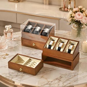 May include: A wooden watch and jewelry storage set featuring a clear acrylic lid, a three-slot watch display case with a pull-out drawer, and a separate open-top tray with ring rolls and a compartment for small accessories, all lined in cream fabric.