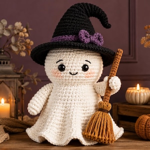 May include: A white crocheted ghost doll wearing a black witch hat with a purple bow. The ghost has black safety eyes, a small stitched smile, and pink blush on its cheeks. It holds a brown crocheted broomstick in one hand, featuring a textured handle and a fringed base.